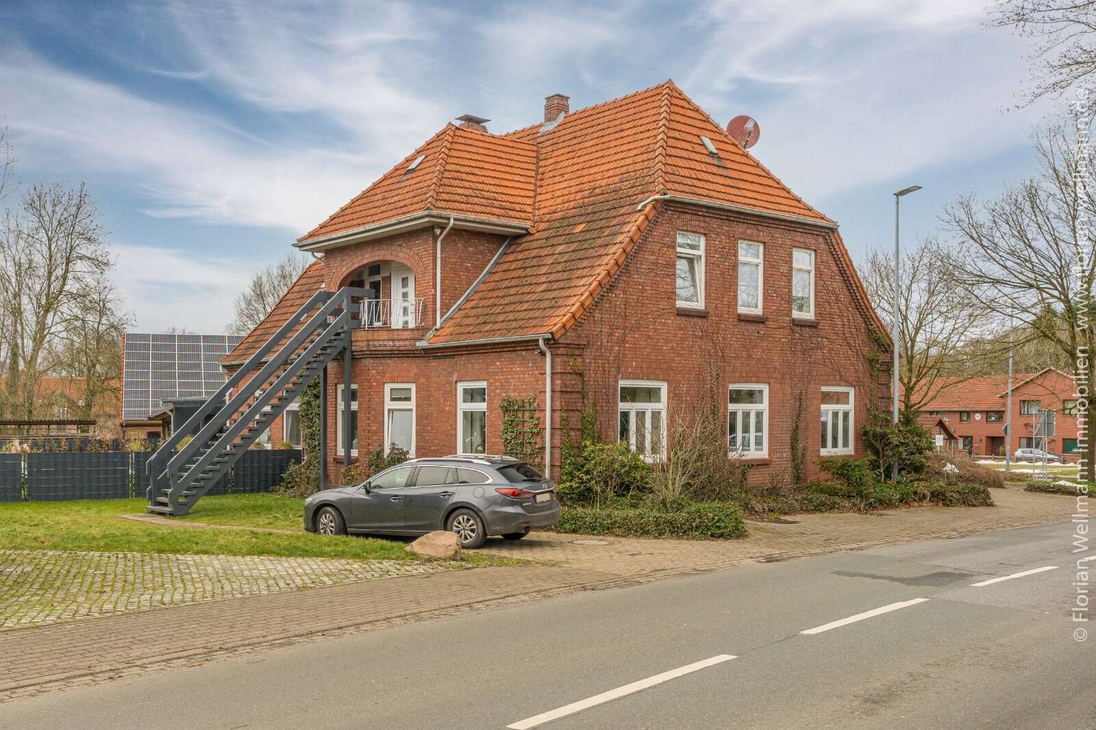 Backsteinhaus mit altem roten Ziegeldach und außenliegender Metalltreppe vor der energetischen Sanierung.
