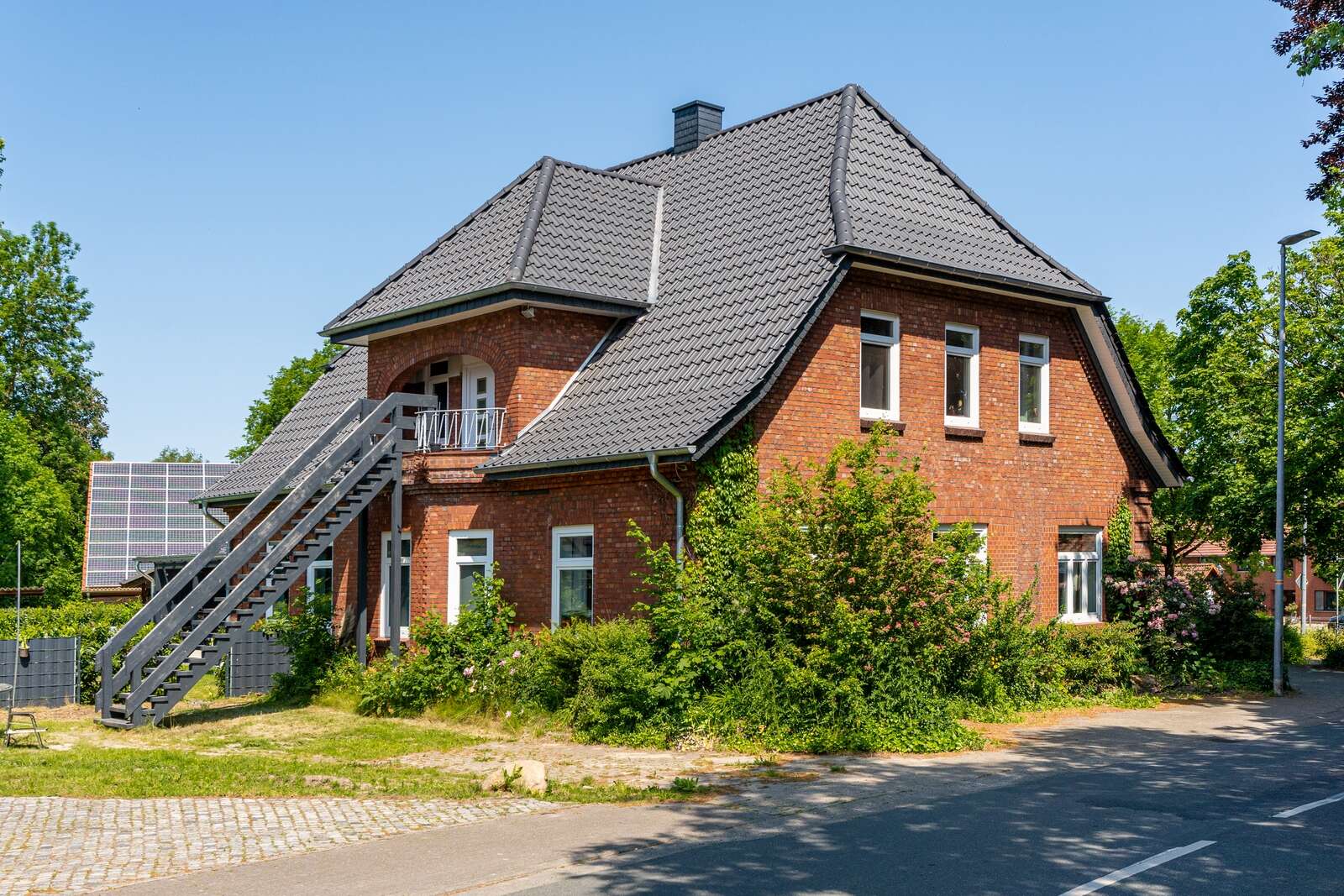 Backsteinhaus nach energetischer Dachsanierung mit neuem dunkelgrauen Ziegeldach und gepflegter Außenanlage.
