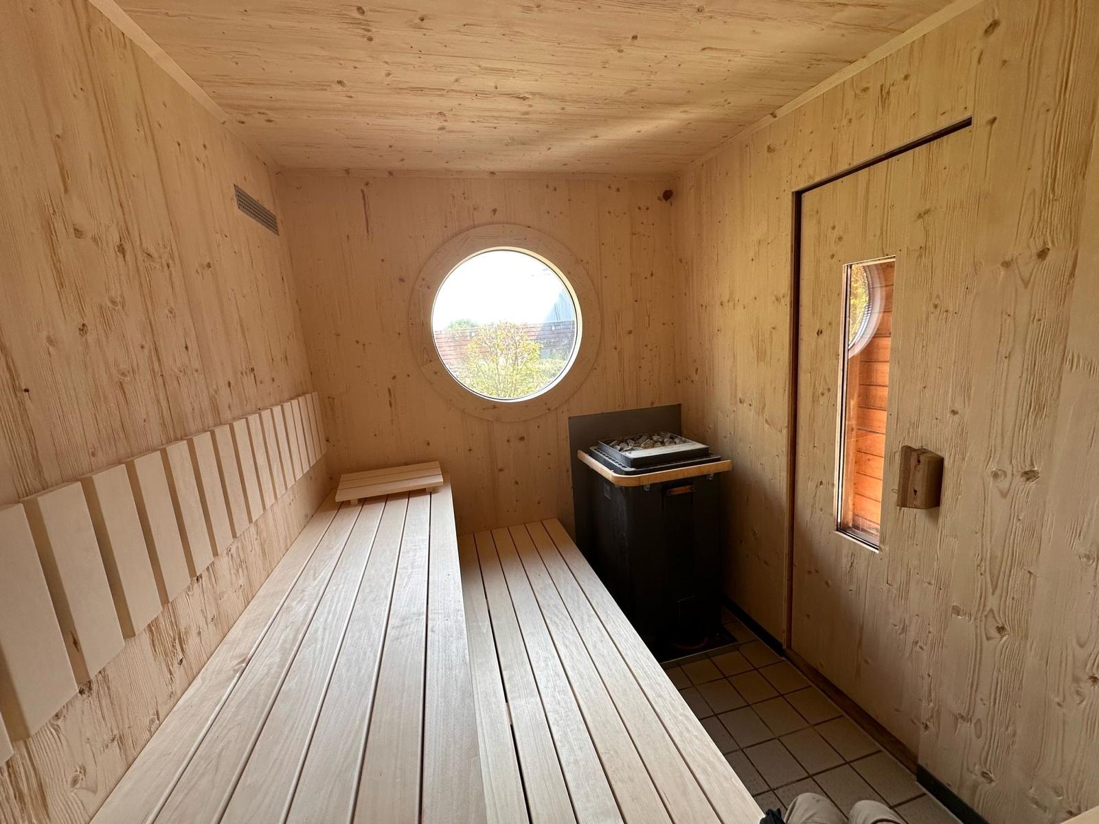 Sauna nachher: helle Holzverkleidung, runde Fensteröffnung, neue Rückenlehnen und ebene Bankflächen